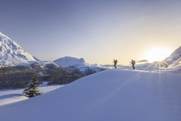 Hikers on snowshoes adventure in deep snow after a heavy snowfall over the frozen lakes of the Engadine. Canton of Graubunden. Maloja Pass. Engadine. Switzerland. Europe