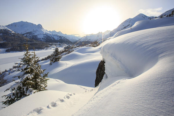 A sun veiled by the mists illuminates the footprints left by snowshoers at the Maloja Pass. Canton of Graubunden. Engadine. Switzerland. Europe