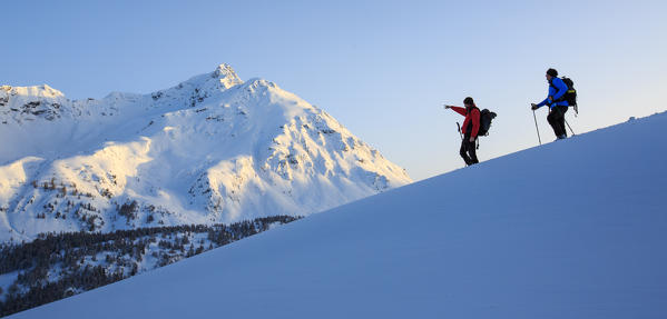 Hiker on snowshoes look at Piz de la Margna lit by the last sun of the day. Canton of Graubunden. Maloja Pass. Engadine. Switzerland. Europe