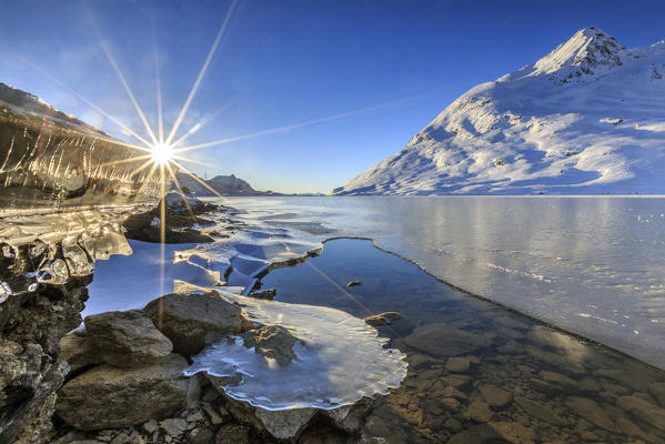 The sun shines over the frozen surface of Lake Bianco of Bernina. Canton of Graubunden. Engadine. Switzerland. Europe