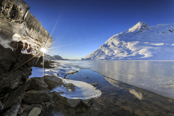 The sun shining through icicles on the shores of Lake Bianco of Bernina frozen. Canton of Graubunden. Engadine. Switzerland. Europe