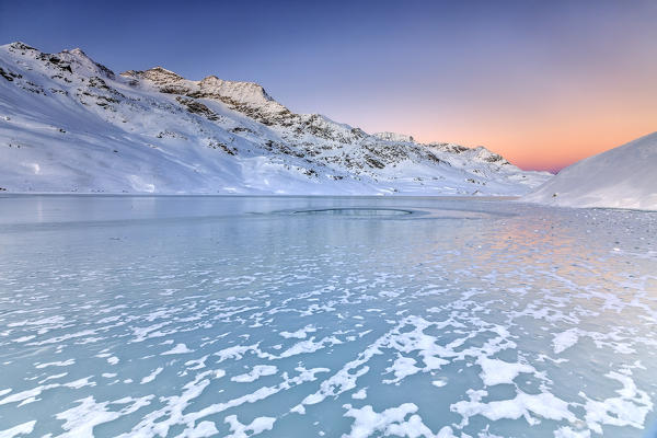 Surface of Lake Bianco of Bernina enhanced by soft colors of dawn. Canton of Graubunden. Engadine. Switzerland. Europe