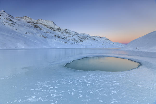Puddle of water not icy yet in the middle of Lake Bianco illuminated by the colors of dawn. Canton of Graubunden. Engadine. Switzerland. Europe