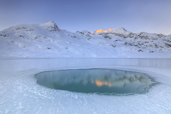 Cambrena peak sunlit reflected in the icy waters of a pond in the center of Lake Bianco of Bernina. Canton of Graubunden. Engadine. Switzerland. Europe