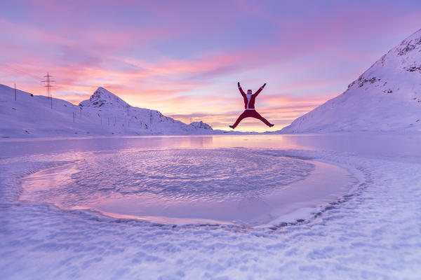 Santa Claus jumps happy on the frozen surface of Lake Bianco at Bernina Pass. Canton of Graubunden. Engadine. Switzerland. Europe