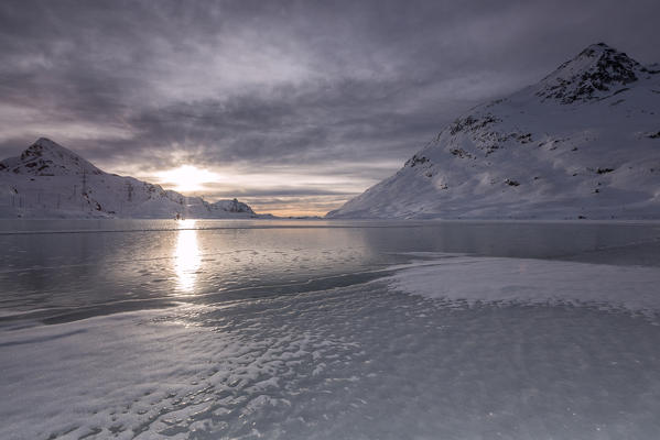 A silvery light illuminates the frozen White Lake at sunrise in a cold winter morning. Bernina Pass. Canton of Graubuenden. Engadine. Switzerland. Europe