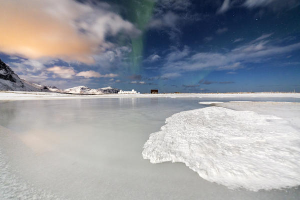 Northern Lights on the frozen sea and snow capped mountains. Flakstad Lofoten Islands Northern Norway Europe