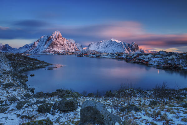 The pink sky at sunrise illuminates Reine village with its cold sea and the snowy peaks. Lofoten Islands Northern Norway Europe