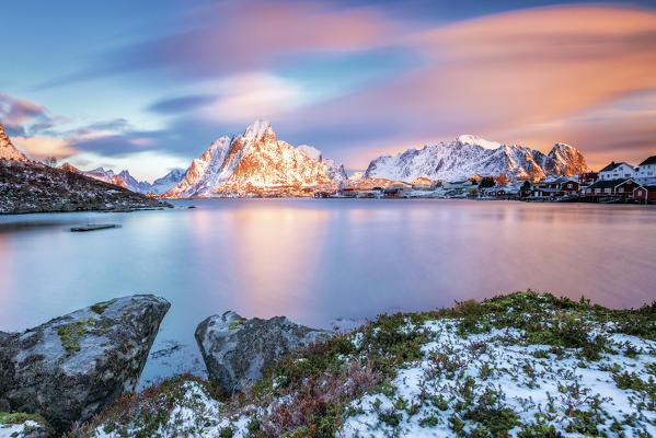 The pink sky at sunrise illuminates Reine village with its cold sea and the snowy peaks. Lofoten Islands Northern Norway Europe