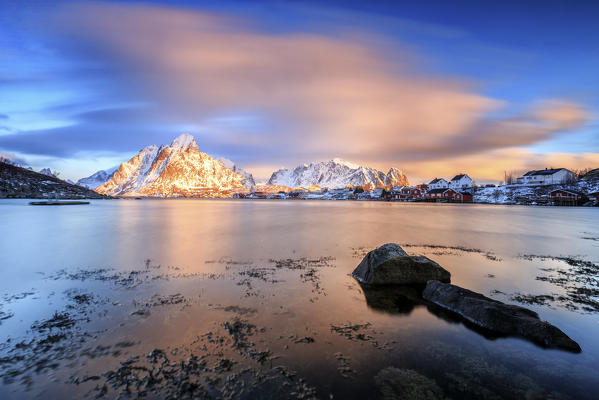 The pink sky at sunrise illuminates Reine village with its cold sea and the snowy peaks. Lofoten Islands Northern Norway Europe