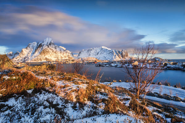 The pink sky at sunrise illuminates Reine village with its cold sea and the snowy peaks. Lofoten Islands Northern Norway Europe