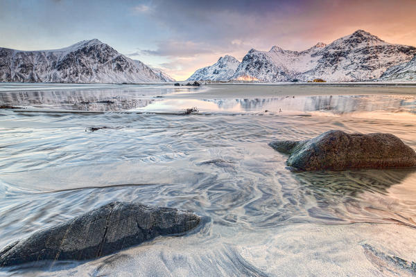 Pink sky on the  surreal Skagsanden beach surrounded by snow covered mountains. Lofoten Islands Northern Norway Europe