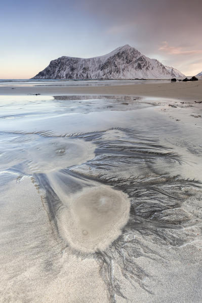 Pink sky on the  surreal Skagsanden beach surrounded by snow covered mountains.  Lofoten Islands Northern Norway Europe