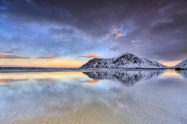 Sunset on Skagsanden beach surrounded by snow covered mountains reflected in the cold sea. Lofoten Islands. Norway Europe