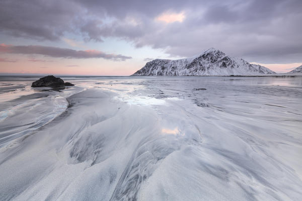 Waves on the  surreal Skagsanden beach surrounded by snow covered mountains. Lofoten Islands. Northern Norway Europe