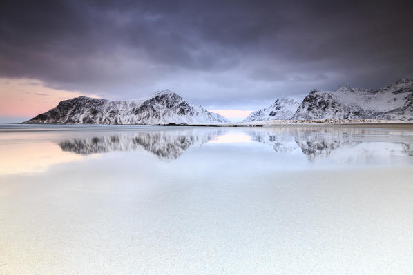 Pink sky and snow covered mountains reflected in the cold sea. Skagsanden. Lofoten Islands Northern Norway Europe