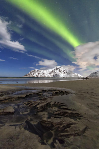 Northern Lights illuminate Skagsanden beach and the snowy peaks. Lofoten Islands Northern Norway Europe