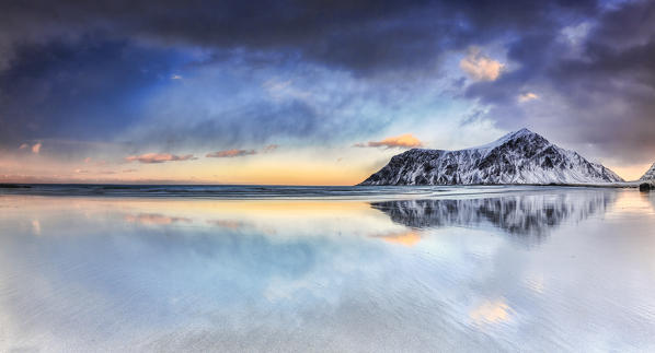 Sunset on Skagsanden beach surrounded by snow covered mountains reflected in the cold sea. Lofoten Islands Norway Europe