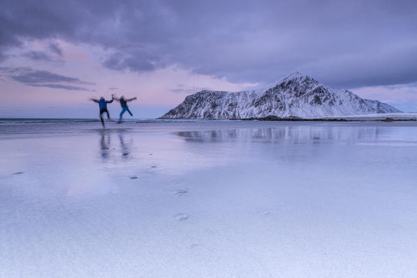 Sunset and hikers on Skagsanden beach surrounded by snow covered mountains. Lofoten Islands Norway. Europe