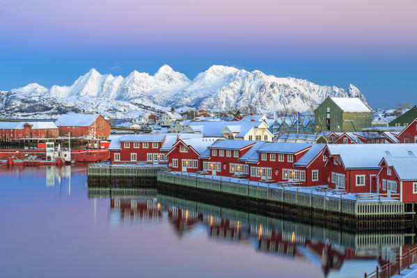 Pink sunset over the typical red houses reflected in the sea. Svollvaer Lofoten Islands Norway Europe