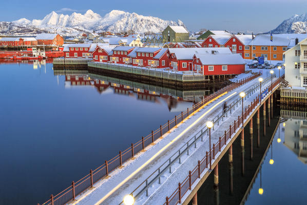 Tourist admire sunset colors on the typical red houses from a deck. Svollvaer Lofoten Islands Norway Europe