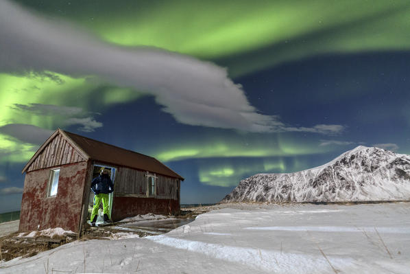 Hiker admire the landscape and the northern lights after resting in a typical house. Flakstad. Lofoten Islands. Norway. Europe