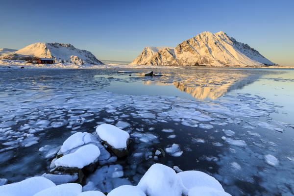 View of the mountains of Gymsøya from Smorten reflected in the clear sea still partially frozen. Lofoten Islands Norway Europe