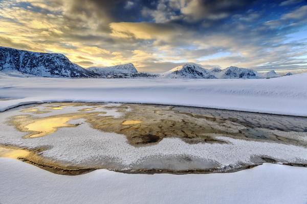 The golden sunrise reflected in a pool of the clear sea where the snow is almost melted. Haukland Lofoten Islands Norway Europe