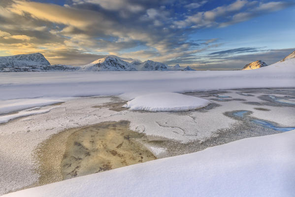 The golden sunrise reflected in a pool of the clear sea where the snow is almost melted. Haukland Lofoten Islands Norway Europe