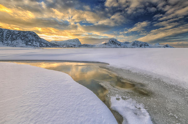 The golden sunrise reflected in a pool of the clear sea where the snow is almost melted. Haukland Lofoten Islands Norway Europe