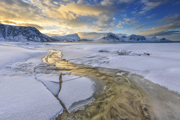The golden sunrise reflected in a pool of the clear sea where the snow is almost melted. Haukland Lofoten Islands Norway Europe