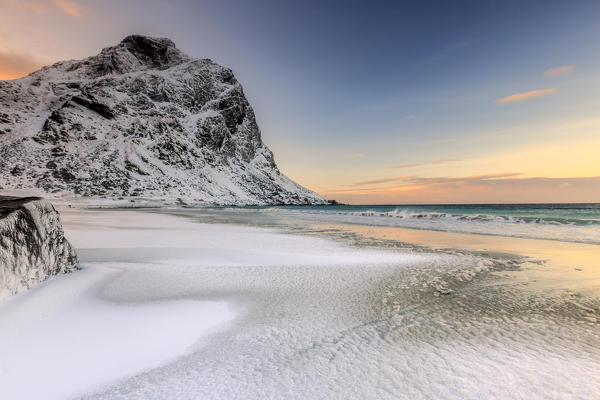 Waves advances towards the shore of the beach surrounded by snowy peaks at dawn. Uttakleiv Lofoten Islands Norway Europe