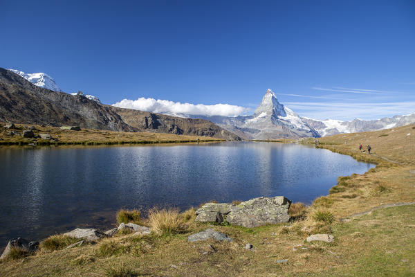 Hikers walking on the path beside the Stellisee with the Matterhorn reflected. Zermatt Canton of Valais Pennine Alps Switzerland Europe