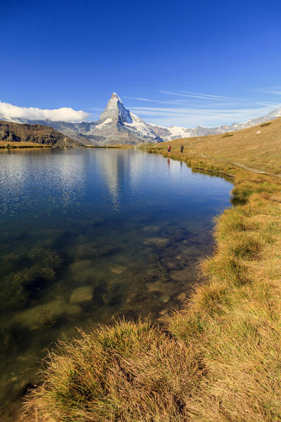 Hikers walking on the path beside the Stellisee with the Matterhorn reflected. Zermatt Canton of Valais Pennine Alps Switzerland Europe