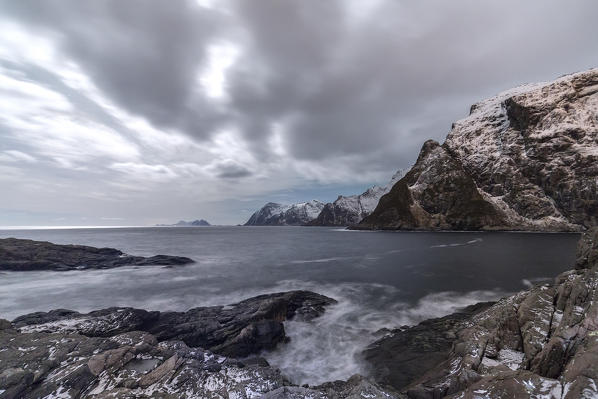 Cloudy sky above the mountains partially snowy and the cold sea. Lofoten Islands. Northern Norway. Europe