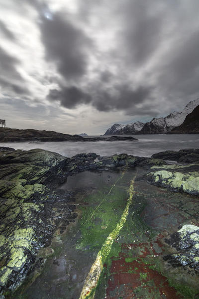 The colors on the rocks contrast with dark clouds above the cold sea. Lofoten Islands. Northern Norway. Europe