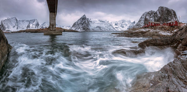 A bridge spans the rough sea and the cliffs with the houses of fishermen. Hamony. Lofoten Islands. Northern Norway. Europe