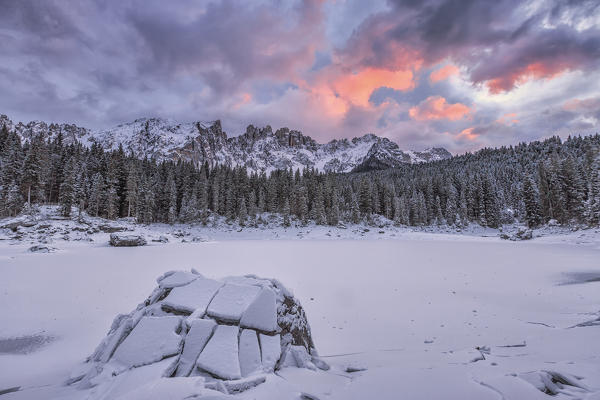 Sunset at Lake Carezza covered with snow in the background the Latemar group. Ega Valley. Dolomites. Trentino Alto Adige Italy