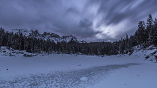 Sunset at Lake Carezza covered with snow in the background the Latemar group. Ega Valley. Dolomites. Trentino Alto Adige Italy