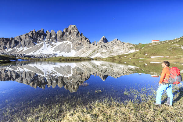 Hiker admires the peaks reflected in Laghi dei Piani.  Sesto Dolomites Trentino Alto Adige Italy Europe