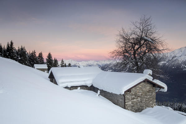 Pink sky at dawn above snow covered huts Tagliate Di Sopra Gerola Valley Valtellina Orobie Alps Lombardy Italy Europe