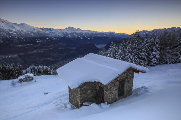 Lights of dawn on snow covered huts and trees Tagliate Di Sopra Gerola Valley Valtellina Orobie Alps Lombardy Italy Europe