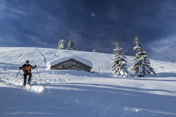 Snowshoe hiker walking near snow covered hut  Motta di Olano Gerola Valley Valtellina Orobie Alps Lombardy Italy Europe