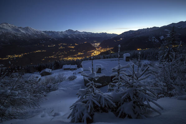 Lights of dusk illuminate the valley and the snow covered huts Tagliate Di Sopra Gerola Valley Valtellina Lombardy Italy Europe