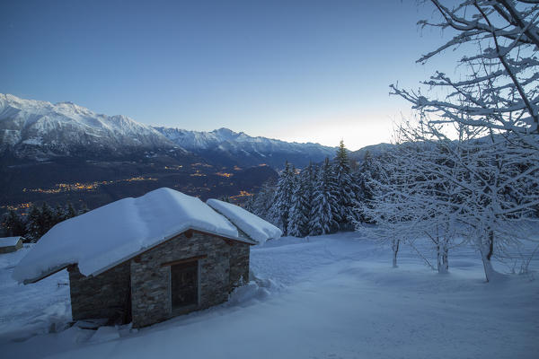 Lights of dusk illuminate the valley and the snow covered huts Tagliate Di Sopra Gerola Valley Valtellina Lombardy Italy Europe