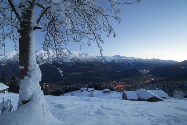 Lights of dusk illuminate the valley and the snow covered huts Tagliate Di Sopra Gerola Valley Valtellina Lombardy Italy Europe