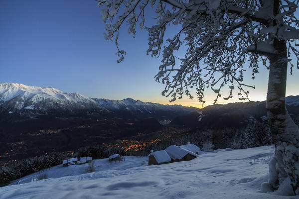 Lights of dusk illuminate the valley and the snow covered huts Tagliate Di Sopra Gerola Valley Valtellina Lombardy Italy Europe
