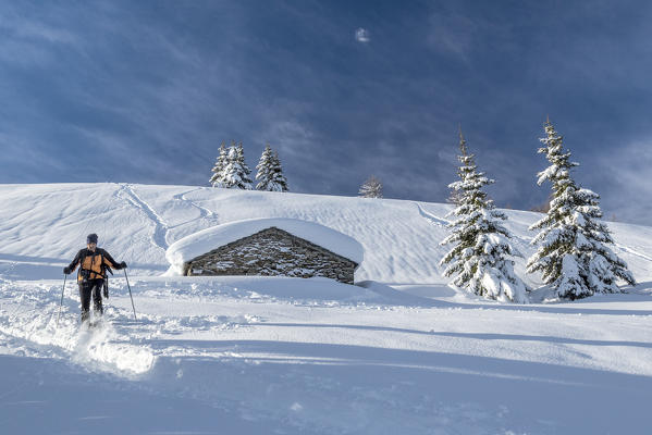 Snowshoe hiker walking near snow covered hut  Motta di Olano Gerola Valley Valtellina Orobie Alps Lombardy Italy Europe