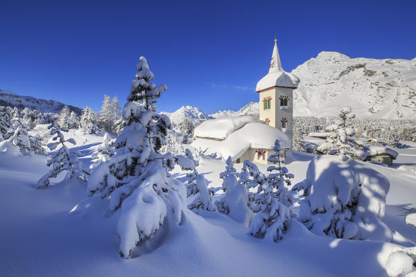 The winter sun illuminate the snowy landscape and the typical church Maloja Canton of Graubünden Engadine Switzerland Europe