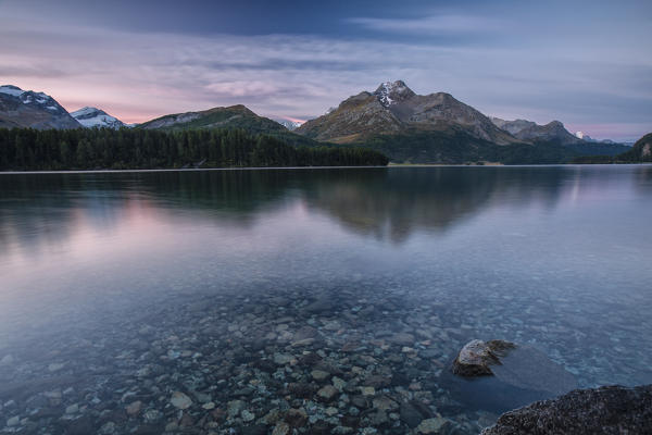 Dawn illuminates the peaks reflected in the calm waters of Lake Sils Engadine Canton of Graubünden Switzerland Europe